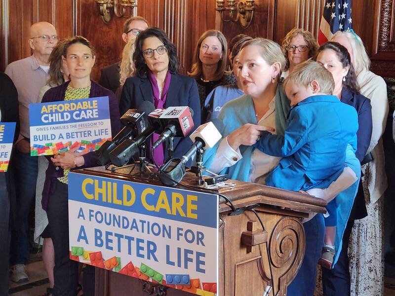 State Sen. Kelda Roys, holding her toddler, speaks about legislation Democrats are proposing to provide ongoing funding for child care providers. (Photo by Erik Gunn/Wisconsin Examiner)