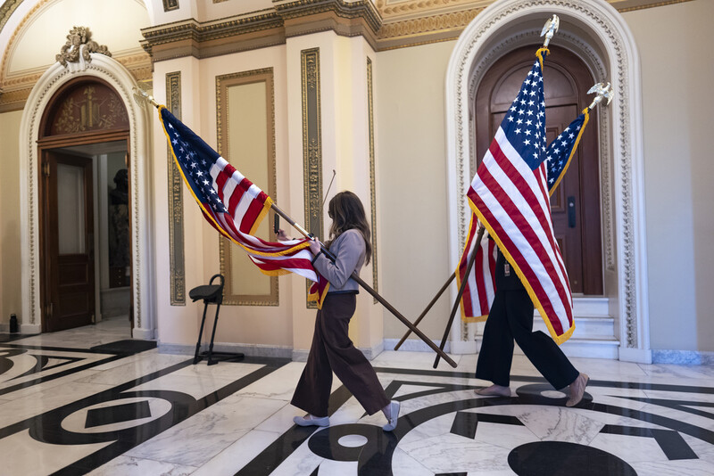 House staffers carry American flags through a corridor outside the House chamber which will be used for a ceremony with Speaker of the House Mike Johnson, R-La., after final passage of President Donald Trump's signature bill of tax breaks and spending cuts, at the Capitol in Washington, Thursday, July 3, 2025. (AP Photo/J. Scott Applewhite)