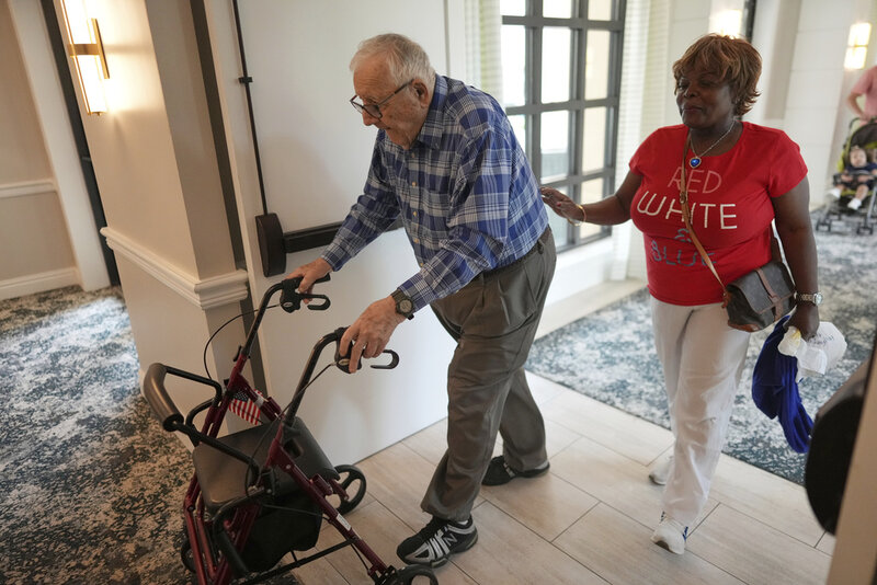 Resident Eugene Preslier, right, is accompanied by his private certified nursing aid Miriam Louis as he returns from a meal to his apartment in the independent living facility at the Toby and Leon Cooperman Sinai Residences, July 4, 2025, in Boca Raton, Fla. (AP Photo/Rebecca Blackwell)