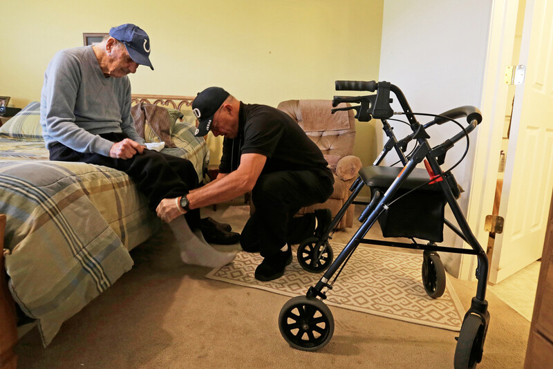 FILE - Caregiver Warren Manchess helping Paul Gregoline with his shoes and socks, in Noblesville, Ind., Nov. 27, 2013. (AP Photo/Darron Cummings, File)