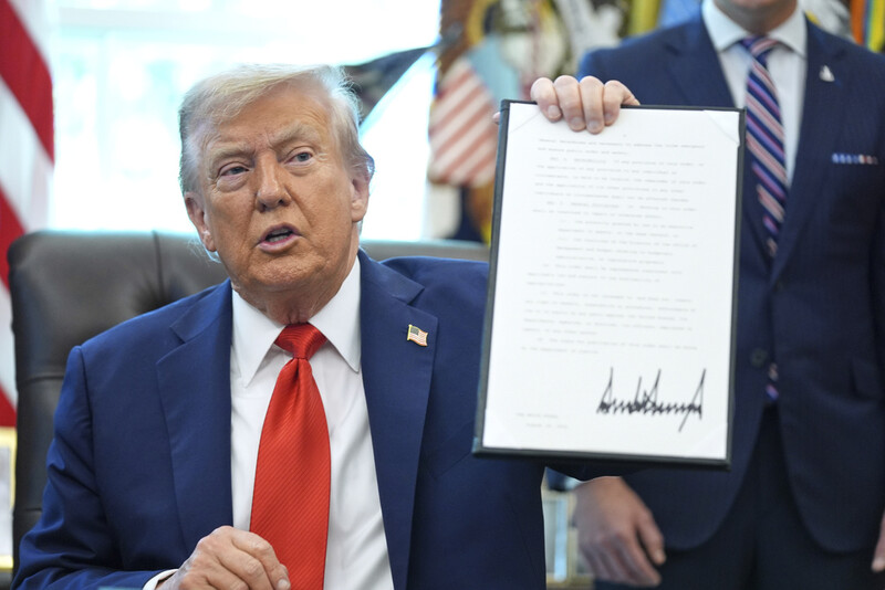 President Donald Trump holds up a signed executive order requiring the Justice Department to investigate instances of flag burning, in the Oval Office of the White House, Monday, Aug. 25, 2025, in Washington. (AP Photo/Evan Vucci)