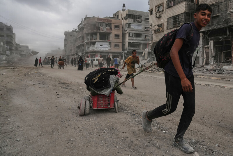 Displaced Palestinians walk with their belongings along the heavily damaged Al-Jalaa Street in Gaza City, Sunday, Oct. 12, 2025, after Israel and Hamas agreed to a pause in their war and the release of the remaining hostages. (AP Photo/Abdel Kareem Hana)