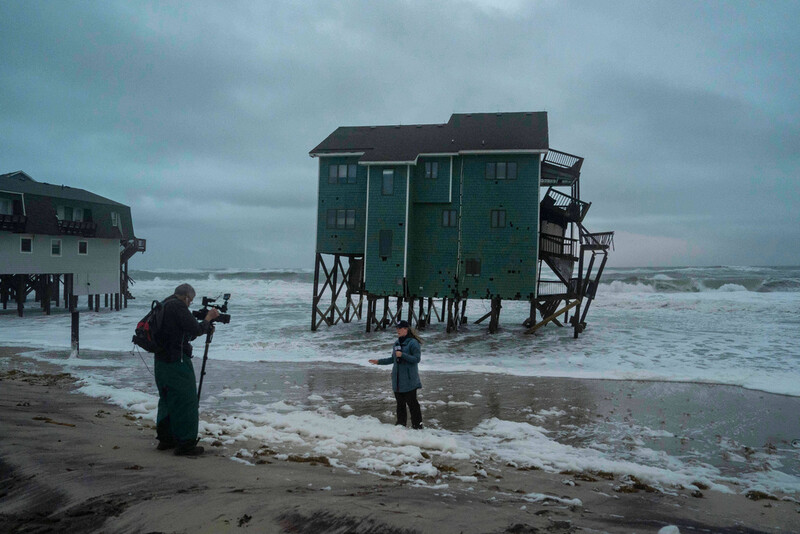 A Fox Weather reporter films in front of a house at risk of collapse in the midst of a storm, Sunday, Oct. 12, 2025, in Buxton, N.C. (AP Photo/Allison Joyce)