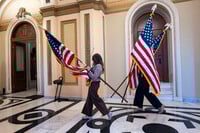 House staffers carry American flags through a corridor outside the House chamber which will be used for a ceremony with Speaker of the House Mike Johnson, R-La., after final passage of President Donald Trump's signature bill of tax breaks and spending cuts, at the Capitol in Washington, Thursday, July 3, 2025. (AP Photo/J. Scott Applewhite)