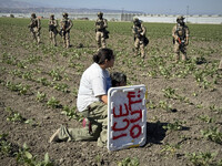 FILE - A demonstrator kneels in front of federal agents in a farm field during an immigration raid in Camarillo, Calif., Thursday, July 10, 2025. (AP Photo/Michael Owen Baker, File)