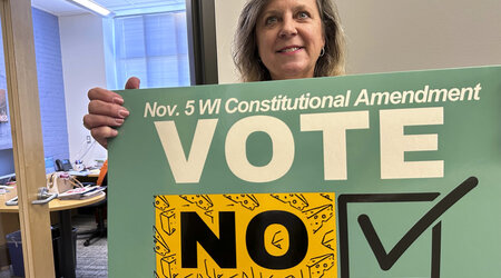 Debra Cronmiller, executive director of the League of Women Voters of Wisconsin, holds a sign outside her Madison office, Wednesday, Oct. 16, 2024, urging voters on Nov. 5 to reject a Republican-authored amendment to the state constitution that would explicitly prohibit foreign nationals from voting in Wisconsin. (AP Photo/Todd Richmond)