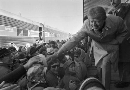 FILE - President-elect Jimmy Carter leans over to shake hands with some of the people riding the &quot;Peanut Special&quot; to Washington, Jan. 19, 1977. They will travel all night, arriving in Washington in time for Carter's inauguration as president on Jan. 20. (AP Photo, File)