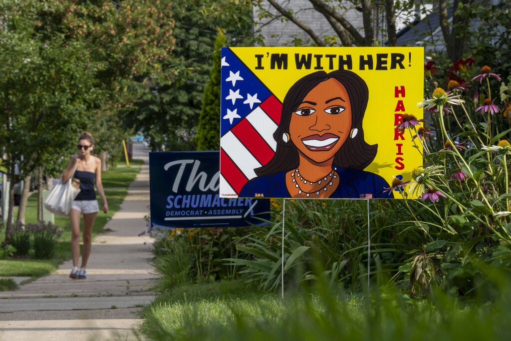 A pedestrian walks along the sidewalk past a sign in support of Kamala Harris on Tuesday, July 30, 2024, in Madison, Wis. (AP Photo/Kayla Wolf)