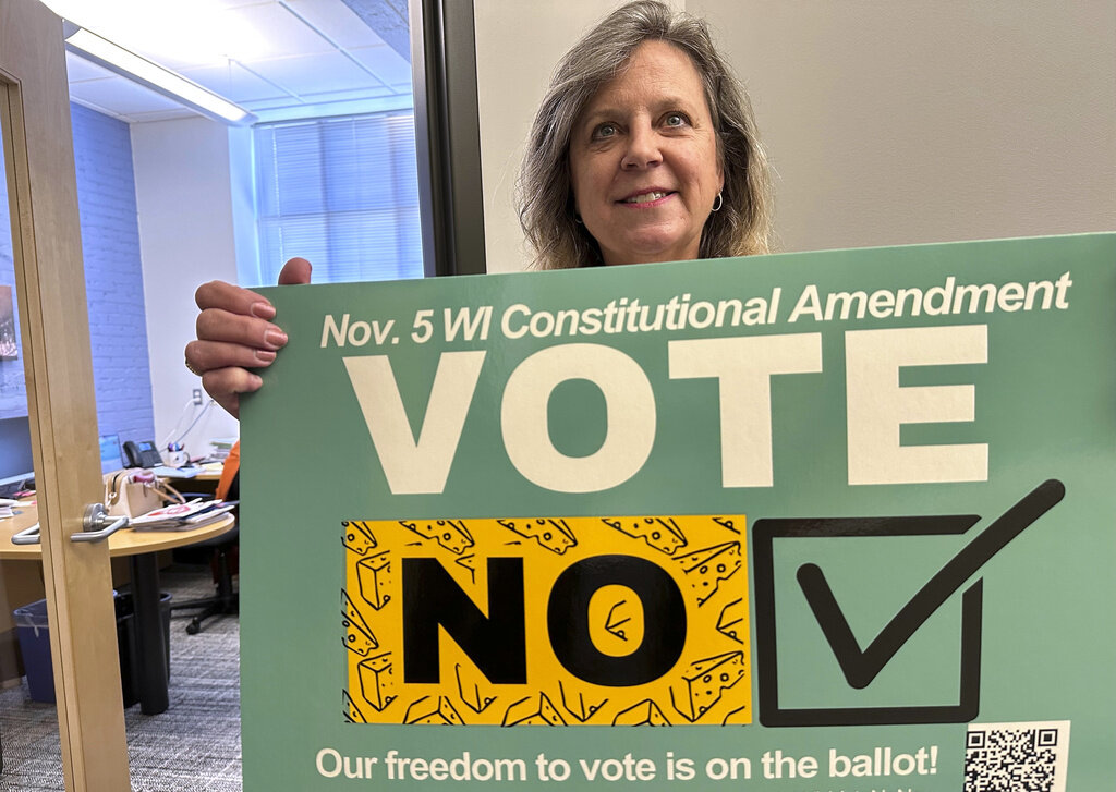 Debra Cronmiller, executive director of the League of Women Voters of Wisconsin, holds a sign outside her Madison office, Wednesday, Oct. 16, 2024, urging voters on Nov. 5 to reject a Republican-authored amendment to the state constitution that would explicitly prohibit foreign nationals from voting in Wisconsin. (AP Photo/Todd Richmond)